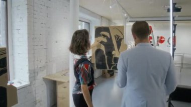 Beyaz kadın ressam ve erkek galeri müdürünün açılıştan önce sergi salonunda sergilenen sanat eserlerini incelerken ve tavandan sarkan sanat eserlerini düzeltirken orta boy tam kare.