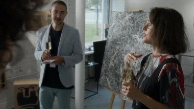 Modern sanat galerisindeki şahsi sergide yeni başyapıtını sergileyen beyaz kadın sanatçının, fikirleri, kavramları ve yaratıcı süreçleri ekran dışı ziyaretçilere açıklayan orta büyüklükte bir resmi.