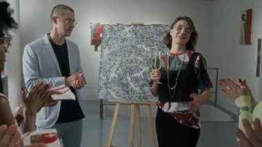 Modern sanat galerisindeki yeni sanat sergisinde, şampanya resepsiyonundaki konukları alkışlayan, parıldayan kameralarla yeni sanat eserlerini sunan beyaz kadın sanatçının orta boy zoom çekimi.