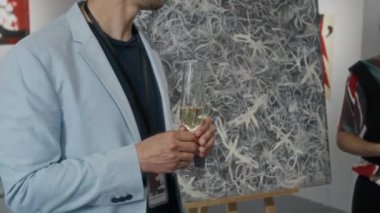 Beyaz tenli yakışıklı erkek sanat eleştirmeninin orta boy yakın çekimi halka yeni çağdaş sanat resimleri hakkında konuşuyor, galerideki sergide sergileniyor, şampanya partisinde