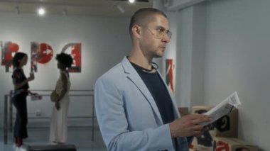 Broşürde bilgi okurken, kavramsal sanat eserleri veya galeride bulunan broşürlü yakışıklı beyaz erkek ziyaretçinin orta boy fotoğrafı.
