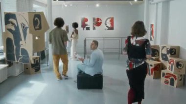 Çok ırklı ziyaretçilerin galerideki çağdaş sanat sergisinde gezinirken çekilmiş geniş bir zaman çizelgesi. Sanat eserlerine hayran olmak, akıllı telefon kullanmak, puffe üzerinde oturmak, bilgi broşürleri okumak.