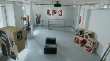 Çağdaş sanat galerisi veya müzesinde, beyaz tuğla duvarları olan, soyut yüz şekilleri ve resimlerle süslenmiş mukavva kutular yerleştirilmiş, sergilenmeye hazır hiç kimse yok.