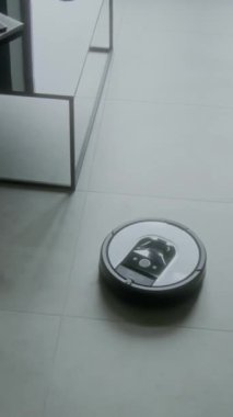 Hiçbir insan, modern aile evindeki gri taşlı zeminde hareket eden, toz ve kiri temizleyen evcil robot vakumunu dikey olarak takip etmez.