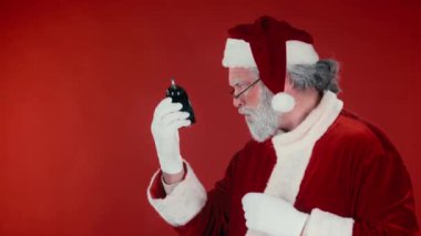 Geleneksel kostümle Noel Baba 'yı acele ettirirken, alarm saatine bakarken ve kırmızı arkaplanda zamanı gösterirken, saat 5' ten 12 'ye kadar, şablon veya kopyalama alanı.