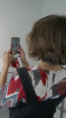 Modern sanat müzesinde resimlerin önünde dikilen, sanat eserlerine hayran olan, akıllı telefondan fotoğraf çeken anonim bir kadının dikey arka planı.