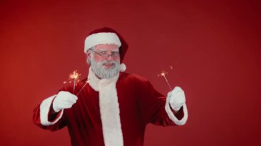 Geleneksel kostümlü neşeli Noel Baba 'nın kırmızı arka planda yanan havai fişeklerle dans edip kameraya bakarken orta büyüklükte bir portresi. Şablon için uygun, alanı kopyala