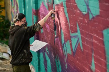 Açık havada yeni bir grafiti başyapıtı üzerinde çalışırken duvara pembe boya uygulayan genç yaratıcı bir adam.