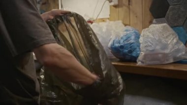 Tanınmayan erkek plastik geri dönüşüm tesisi işçisinin orta ölçekli fotoğrafları sıralanmış şişe kapaklarını topluyor, siyah çöp torbasını alıp götürüyorlar.