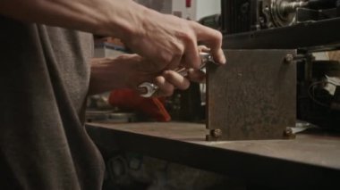 Metal parçaları atölyede birleştiren tanınmayan erkek tamircinin elleri, ingiliz anahtarı ve döner vidayla cıvataları metal torna atölyesinin yanındaki atölyede sıkılaştırıyor.