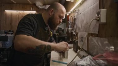 Orta boy dövmeli beyaz erkek plastik geri dönüşüm fabrikası işçisi yeni kesilmiş ekstrüder kalıbının prototipini kontrol ediyor, kalibre ile ölçüyor, sonra da duvara teknik çizimlere numara yazıyor.