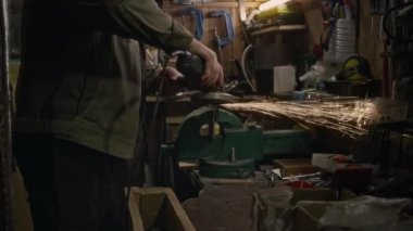 Sakallı, beyaz erkek mühendisin ateş geçirmez üniformalı, koruyucu kulaklık takan, garajda elektrikli testere kullanan, parlak kıvılcımlar saçan orta ölçekli fotoğrafı.