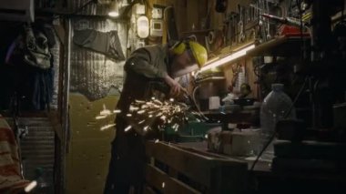 Koruyucu tulumlu, kulaklıklı, metal ya da çelik kenarlı elektrikli testereli, loş ışıklandırılmış, parlak kıvılcımlar saçan, orta boy erkek teknisyen.