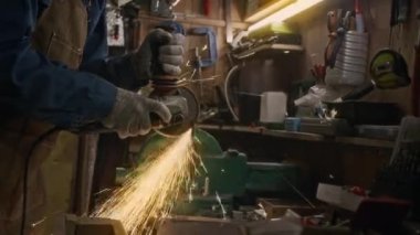 Orta boy eller ve kot gömlekli, önlüklü, çelik testereli çelik kesen eldivenli sanayi işçisinin orta boy görüntüsü garajdaki atölyede, kıvılcım yağmuru altında bekletiliyor.