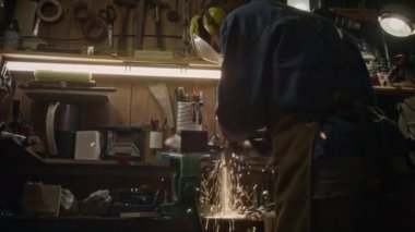 Tanınmayan koruyucu kıyafetli, metali sıkıca kesen, muhteşem uçan kıvılcımlar saçan, endüstriyel tesislerde tek başına çalışan bir adamın orta boy arka çekimi.