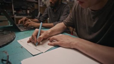 Asyalı genç, beyaz tenli teknisyenin taslak geliştirirken yeni ürünün özelliklerini yazarken orta boy fotoğrafı ve dizüstü bilgisayarda yazı yazan Asyalı erkek meslektaşı.