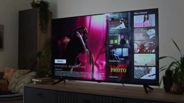 Modern apartmandaki çekmecelerin çekmecesinde kaktüs saksısı yakınında plazma TV ekranında çeşitli filmlerle yayın yapan kimse yok.