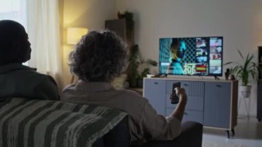 Modern oturma odasındaki koltukta oturan ve TV 'de film seçen kocanın karısına arkadan sarılmasının arka planı.