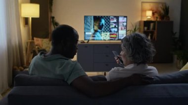 Orta yaşlı karı ve kocanın akşamları televizyon izlemesini, film izlemeyi tercih etmesini, modern oturma odasındaki işten sonra kanepede oturup kucaklaşmasını.