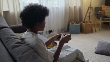 Küçük siyahi çocuğun kanepede oturmuş plazma TV 'de atış oyunu oynarken ki görüntüsü.