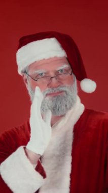 Dikey göğüs hizasında, neşeli, enerjik Noel Baba 'nın kamera ve dansa bakarken, el sallarken, modern dans hareketleri yaparken, kırmızı arka plan, şablon ya da uzay kopyası karşısında eğlenirken,