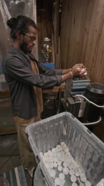 Korumalı gözlüklü Asyalı erkek geri dönüşüm fabrikası işçisinin dikey yan görüntüsü polietilen plastik kapakları öğütücüye yerleştirip taneleri öğütüyor.