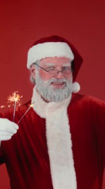 Geleneksel kostüm giymiş neşeli Noel Baba 'nın kırmızı arka planda yanan havai fişeklerle dans edip kameraya bakarken orta boy dikey portresi. Şablon için uygun, alanı kopyala