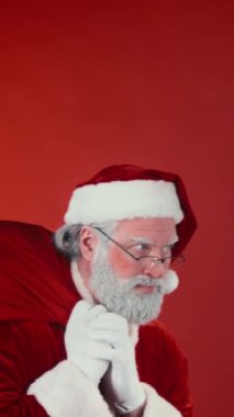 Geleneksel kostümlü sessiz Noel Baba 'yı dikey göğsünden bıçaklayıp kırmızı arka planda, Noel zamanı çocuklara dağıtmak için bir çuval hediyeyle geçerken çekeceğiz. Şablon, boşluğu kopyala