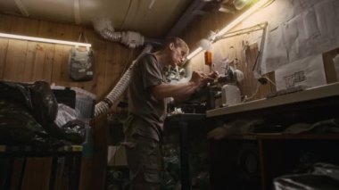 Erkek teknisyenin küçük plastik geri dönüşüm fabrikasında metal torna tamir ederken orta açılı bir çekimi. Duvarda teknik taslaklar, ekstrüzyon kalıpları ve masa üzerinde sıralanmış atık polietilen.