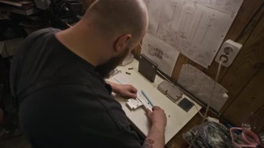 Yüksek açılı orta omuzlu, metal ürünü kalibreli ölçen ve sonra kağıt parçasına ölçümler yazan, dövmeli bir erkek mekanikçinin fotoğrafı.