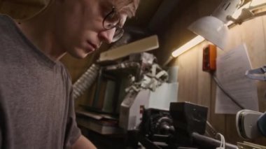 Geceleri garajda tek başına çalışırken torna kesme ve cıvatalarla tamir etme bileşenlerini birleştiren gözlüklü genç beyaz erkek mekanikerlerin ellerini ve yüzünü yana yatırdı.