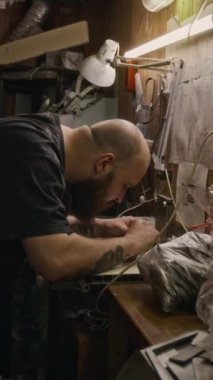 Beyaz önlüklü genç erkek mühendisin kalibre ile yeni kesilmiş metal parçaları kontrol ederken orta boy dikey görüntüsü, kağıt ya da listeye ölçümler yazarken.