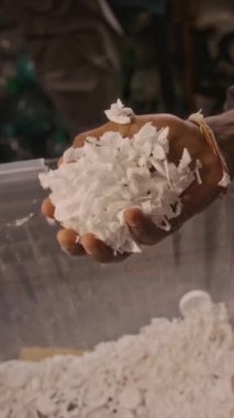 Tanınmayan bir atölyede çalışan bir avuç dolusu geri dönüşümlü polietilen plastik tanecikleri kutudan alıp geri dönüşüm fabrikasında incelerken dikey çekimde çekilmiş.