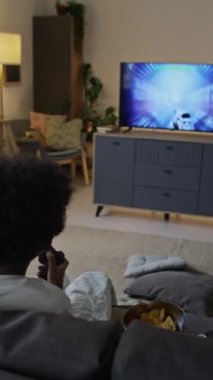 Küçük çocuğun kanepede kontrolörle oturduğu ve evde yalnız başına video oyunu oynadığı dikey bir sahne.