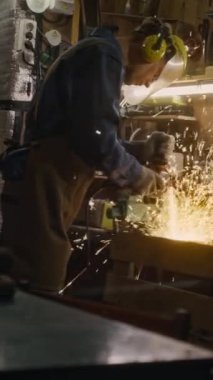 Erkek teknisyenin eldivenli, kulaklı, kasklı ve yüz kalkanlı tam dikey görüntüsü. Atölyede veya araba tamirhanesinde çelik kesiyor. Muhteşem kıvılcımları var.