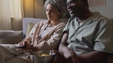 Mutlu, orta yaşlı ve evli çiftin evde televizyon izlemekten zevk almaları, kocanın karısına arkadan sarılmaları, birlikte boş zaman geçirmeleri.