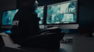 Alışveriş veya iş merkezinin kontrol odasındaki sabit hat telefonunun yakın çekim görüntüsü ve alıcıyı alan ve anormal müşteri davranışlarını bildirmek için meslektaşlarını arayan erkek güvenlik görevlisinin eli.