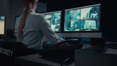Beyaz kadın güvenlik görevlisinin otelin ya da iş merkezinin kontrol odasında oturduğu, CCTV kamera görüntülerini izlediği, ev telefonundan yöneticiyi aradığı ve olası bir olayı bildirdiği orta ölçekli bir fotoğraf.