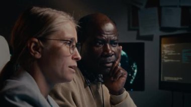 Afrika kökenli Amerikalı erkek bilgi işlem uzmanının, kafkas kökenli genç bayan meslektaşına, ofisinde bilgisayar ekranları önünde yan yana otururken, kodunda dinleme cihazı bulunmasını tavsiye eden yakın plan görüntüleri.