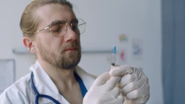 Sakallı beyaz immünolojistin klinikteki hastaya aşı vermeden önce şırıngadaki havayı ilaçla temizlemesi.