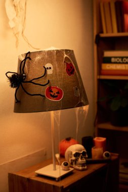 Ürkütücü oyuncak örümcek ve elektrikli lamba üzerinde örümcek ağı insan kafatası, mum ve olgun balkabağı ile küçük bir masada duruyor.