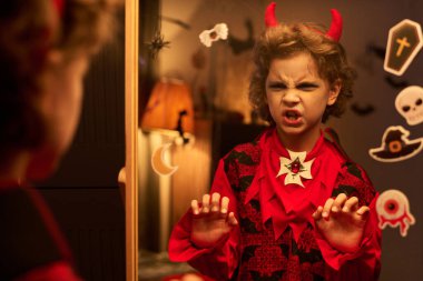 Cadılar Bayramı arifesinde evde aynanın önünde durup kaşlarını çatan ve kaşlarını çatan korkunç çocuk.