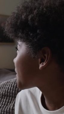 Küçük siyahi çocuğun TV 'de büyüleyici bir film izlerken abur cubur yerken, evde boş vakit geçirirken çekilmiş dikey bir fotoğrafı.