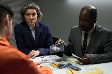 Resmi giysiler içinde turuncu takım elbiseli kişilerle görüşen şahıslar masadaki belgeleri ve kanıtları incelerken...