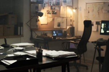 Masaya dağılmış kağıtlarla loş aydınlatılmış ofis ortamını araştırmak ve duvarlara yerleştirilmiş belgeler ve fotoğraflarla dolu ilan panosu