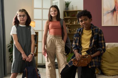 Üç çocuk oturma odasında sırt çantalarını tutuyorlar, her biri eşsiz bir giyim tarzı ve ifadeye sahip, okula gitmeye hazır. Kendinden emin, heyecanlı, gösterişli ve şık görünüyorlar.