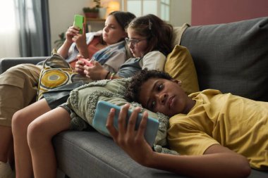 Bir grup genç kanepede uzanmış, akıllı telefonlarını kullanmaya dalmışlar. Rahat atmosferi ve modern mobilyaları olan rahat oturma odası.