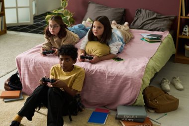 Yatak odasında toplanan üç arkadaş, bir video oyunu oturumunda, yerde ve yatakta oturuyorlardı. Dikkatle oyuna odaklanmışlar, etrafları kitaplar ve aletlerle çevrili.