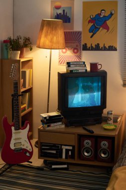 Cozy living room decorated with a mix of retro and modern art, featuring a vintage TV, guitar, wooden lamp, and bookshelf filled with books and plants clipart