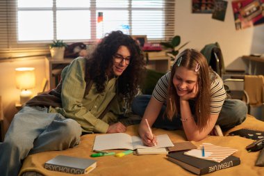 Yatakta oturan öğrenciler, kendilerini işbirlikçi öğrenmeye kaptırmışlar. Kitaplar, defterler ve kırtasiye malzemesi yatağa saçılmış, verimli ve sıradan bir çalışma ortamı yaratıyor.